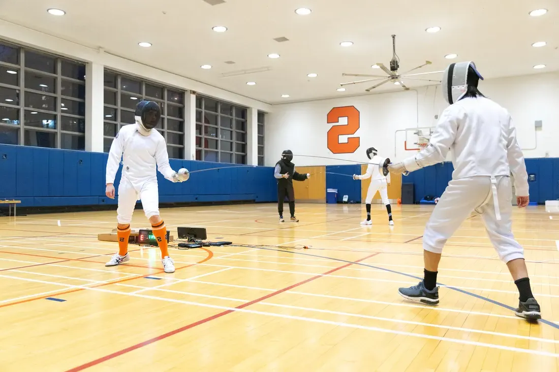 People fencing each other in a Syracuse University gym.